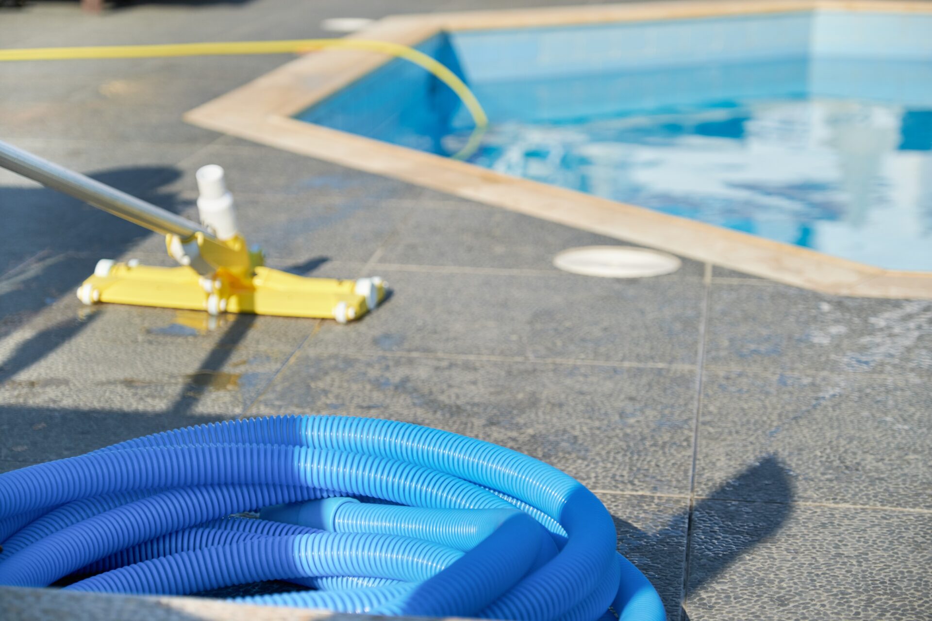 Neben einem Pool liegen Reinigungswerkzeuge, unter anderem ein Schlauch